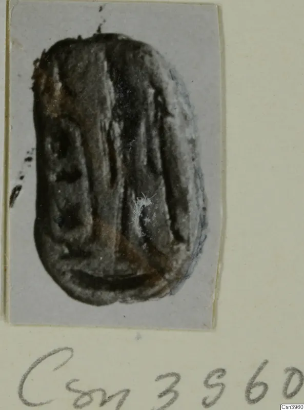 Oval glyptic object, probably a seal or gem, dark and worn with faint engraved lines on its surface