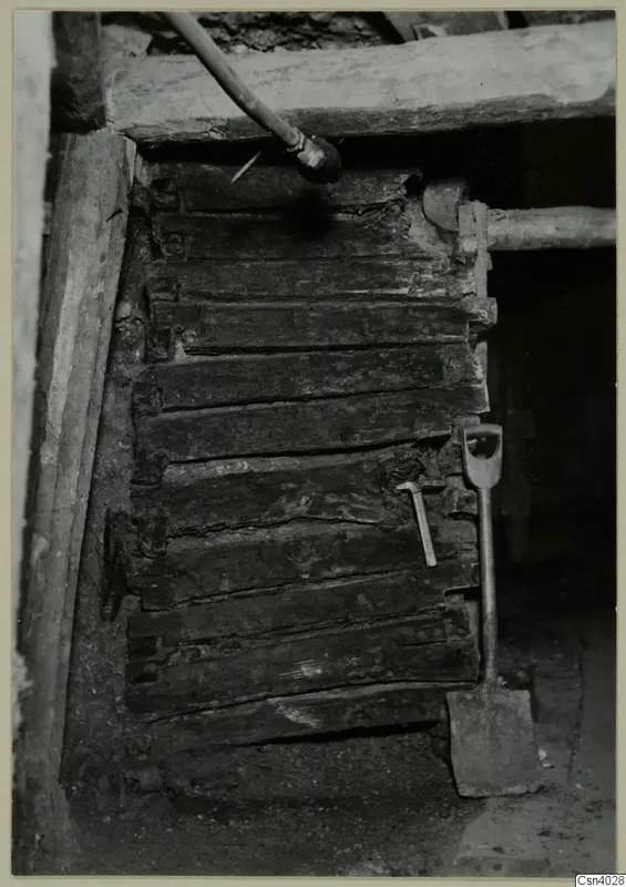 Square timber crib lining of an ancient vertical shaft in a copper mine, with a shovel and hammer beside it