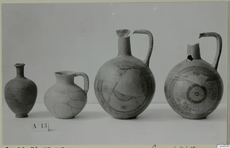 Four pottery vessels of different sizes standing in a row on a pale surface, the two on the right with painted bands and concentric circles