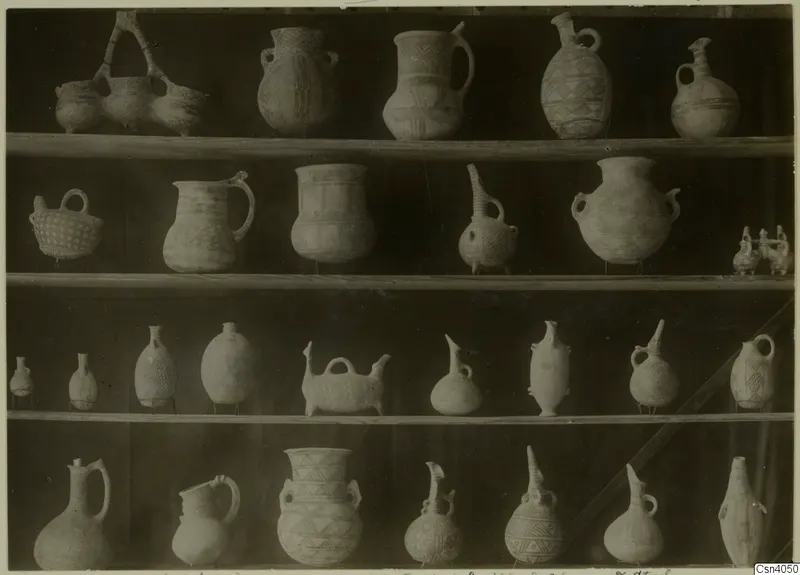 Four shelves of painted pottery jugs, juglets and jars with lattice and diamond patterns, photographed straight on