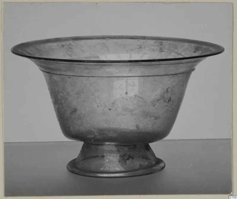 Blown glass bowl on a stemmed foot, with a flared rim, photographed against a grey backdrop.