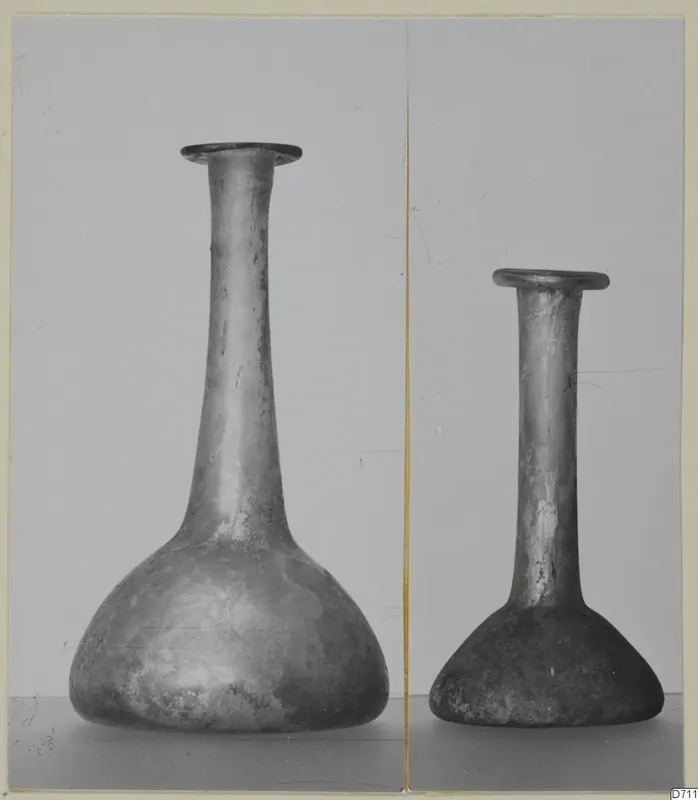 Two blown glass bottles with long necks and flared rims, one noticeably larger than the other.