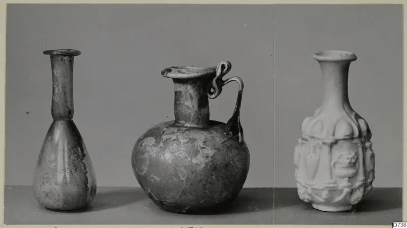 Three small vessels in a row: a slender bottle, a round jug with a loop handle, and a white vessel with moulded relief panels