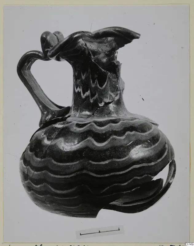 Blown glass jug with wavy light threads and a looped handle, shown with a scale bar.