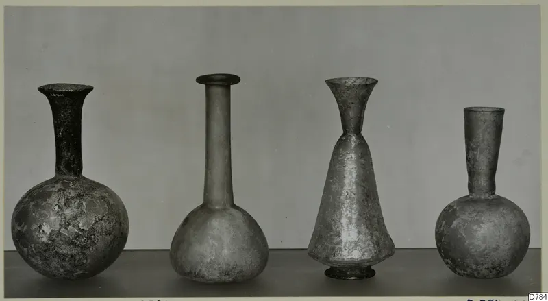Four blown glass bottles with long necks, standing in a row on a dark surface.