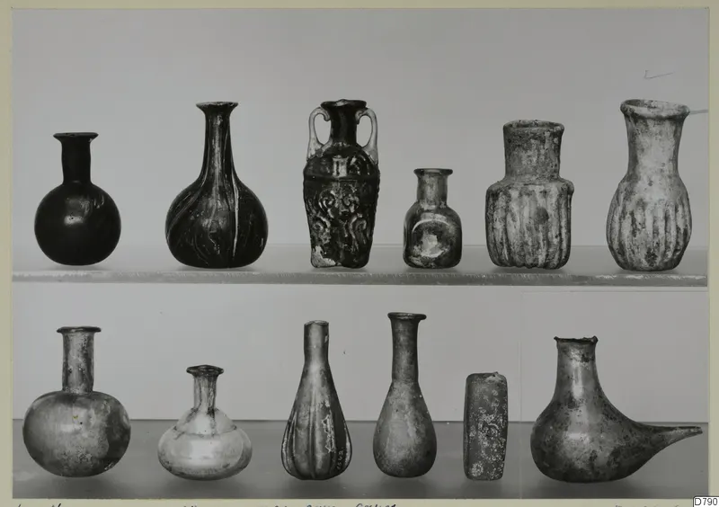 Twelve small blown glass vessels arranged in two rows on shelves