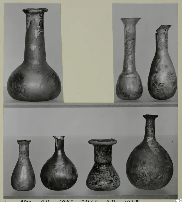 Blown glass vessels with long necks and rounded bodies, shown in two rows on a photo card mount