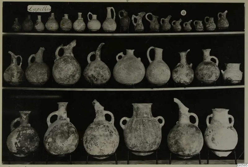 Three shelves of pottery jugs and juglets photographed against a black background