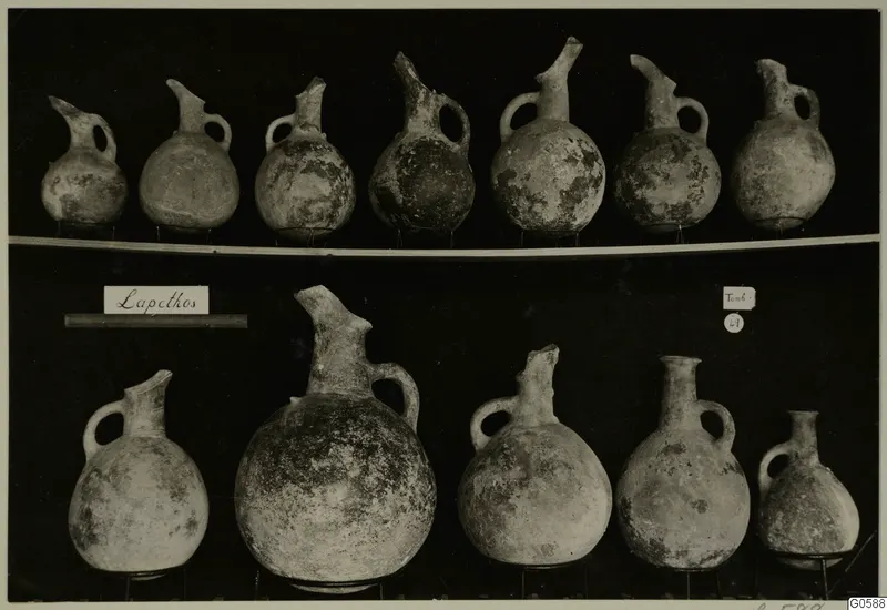 Rows of round juglets with long spouts and loop handles against a dark background, from Lapithos Markides T.49.