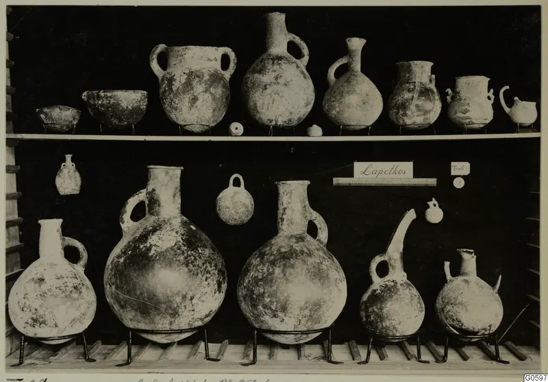 Jugs, bowls and small flasks from Lapithos Markides, T.28, arranged on two shelves against a dark background.