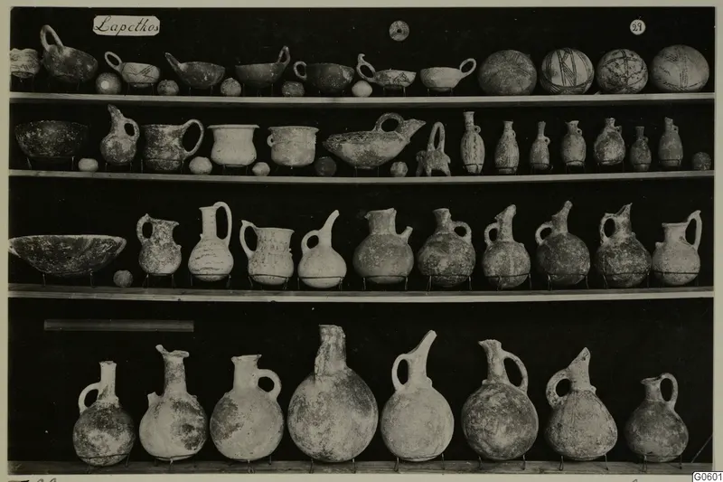 Shelves of pottery jugs, juglets and bowls from Lapithos Markides, T.29, photographed against a black background