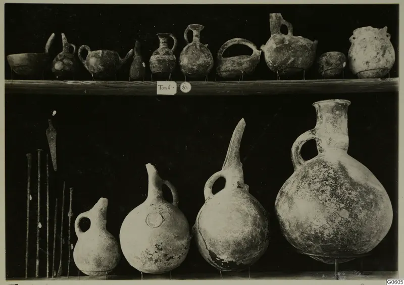Pottery jugs, juglets and bowls from Lapithos Markides on two shelves against a dark background