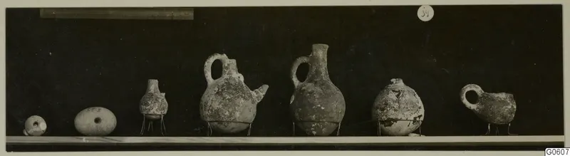 Row of small pottery vessels on a shelf, one with a painted pattern, from Lapithos Markides T.39