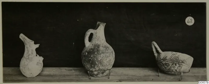 Three pottery vessels from Lapithos Markides, T.42, on a wooden shelf: a broken jug, a handled jug and a painted handled bowl.