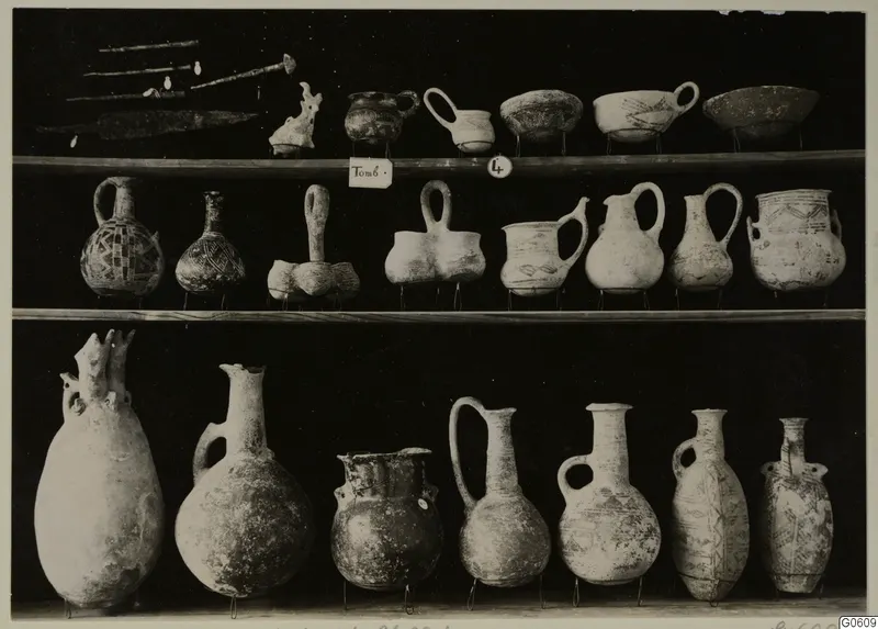 Pottery jugs, bowls and metal objects from T.4 at Lapithos Markides, arranged on three shelves