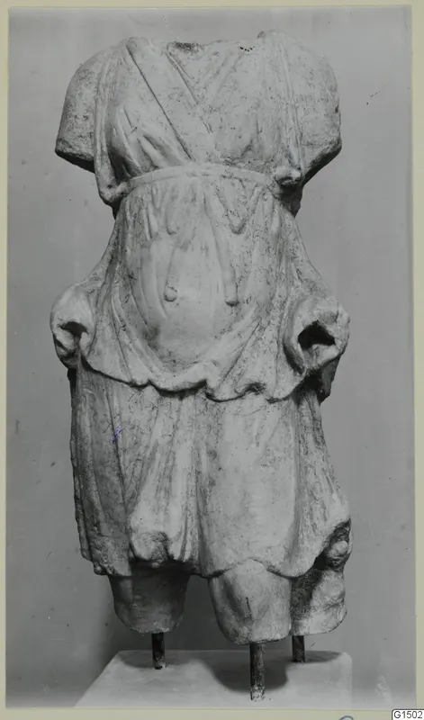 Marble statue of a standing figure, headless and armless, wearing a belted garment, on a metal-supported base.