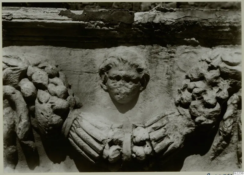 Carved stone relief of a human head between garland swags and draped folds, from a sarcophagus