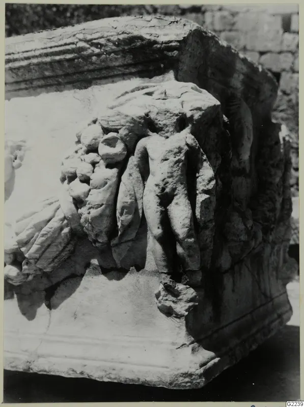 Carved relief on a pale stone block, with a small nude figure among clusters of fruit and drapery folds