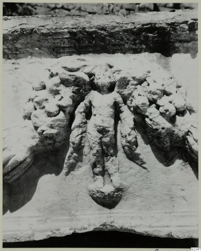 Close view of a carved stone relief showing a small standing figure flanked by scroll-like foliage