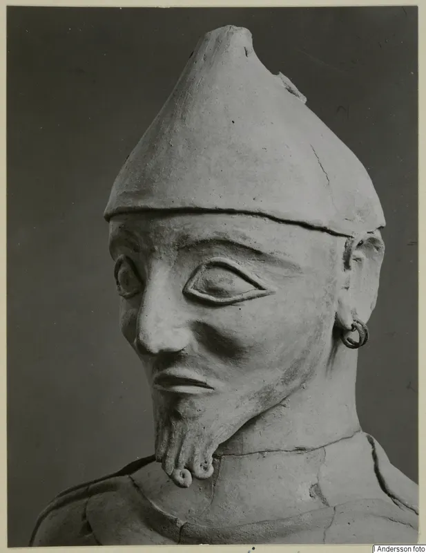 Terracotta statue of a bearded figure in a pointed conical cap, shown head and upper body.