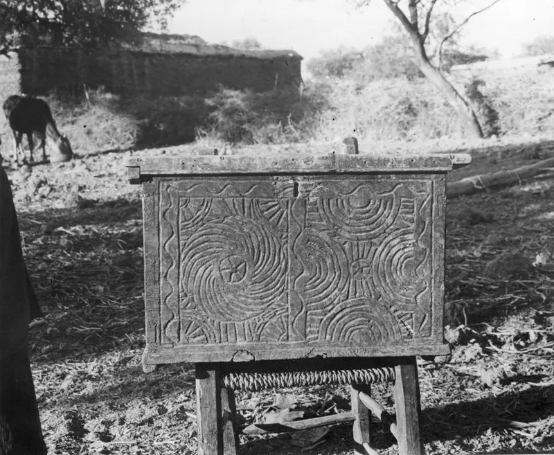 Carved wooden chest on a wooden stand outdoors, its front panel decorated with concentric circles and rosettes