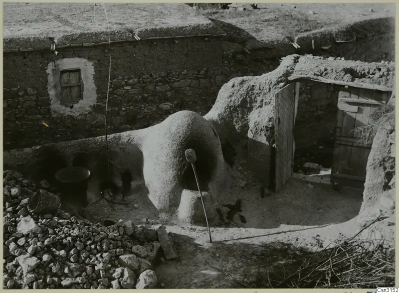 Domed clay bread oven beside a stone-walled house with a wooden door, at Mándres