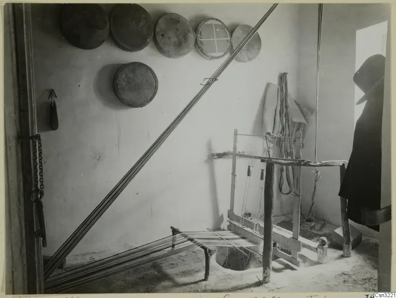 Wooden loom in a whitewashed room at Milia, with round sieves hung on the wall