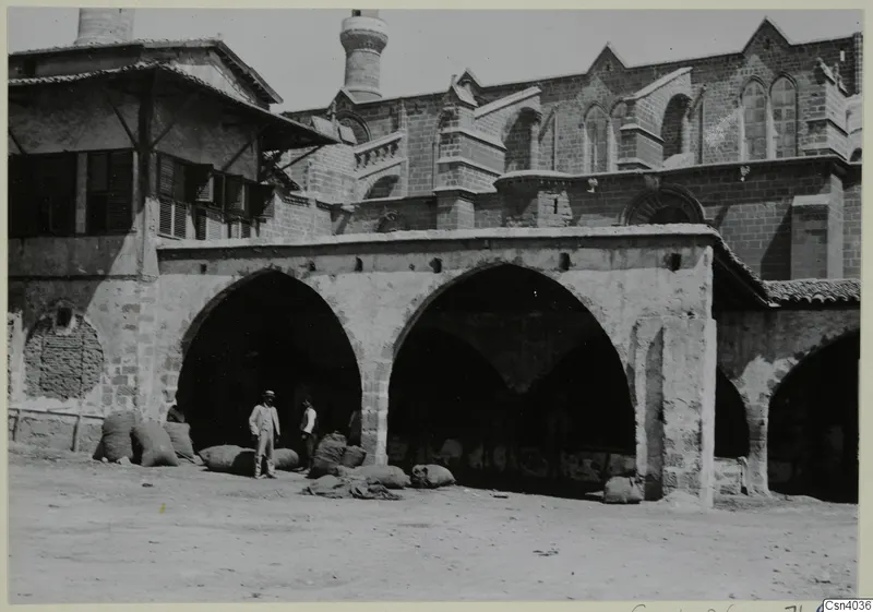 Two men and several sacks beside an arcaded stone building in Nicosia
