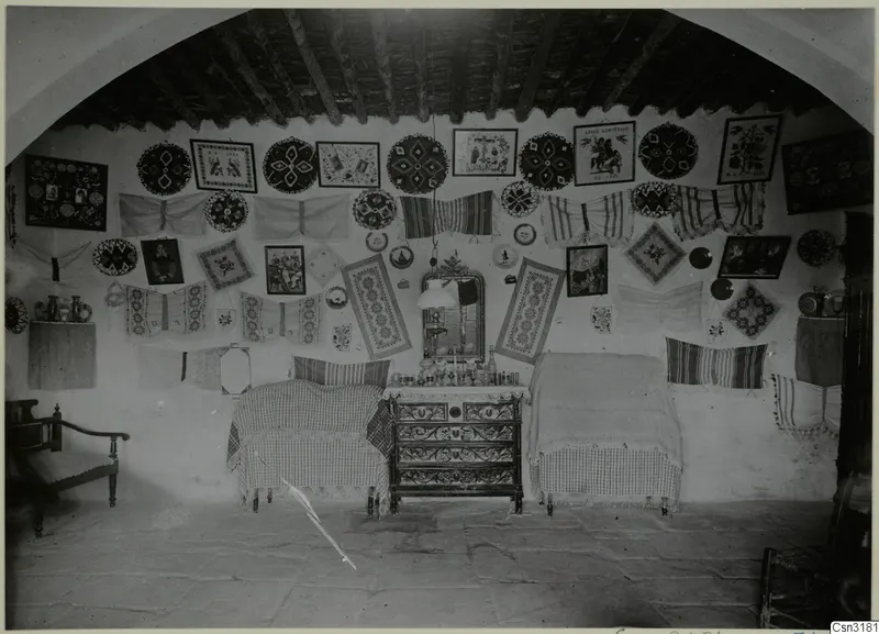 Cottage interior at Milia with embroidered wedding wall hangings, two beds and a carved chest of drawers