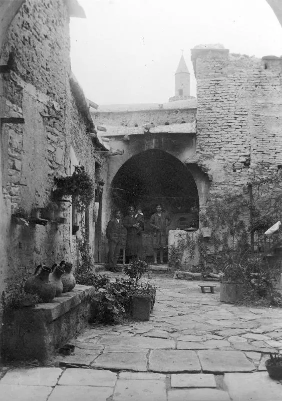 Stone courtyard at Kalavasos with a row of jars on a ledge and people standing in an arched doorway