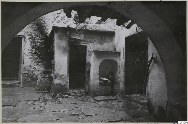 Courtyard of a building seen through a stone arch, with a wall niche holding a jug and a shallow bowl.