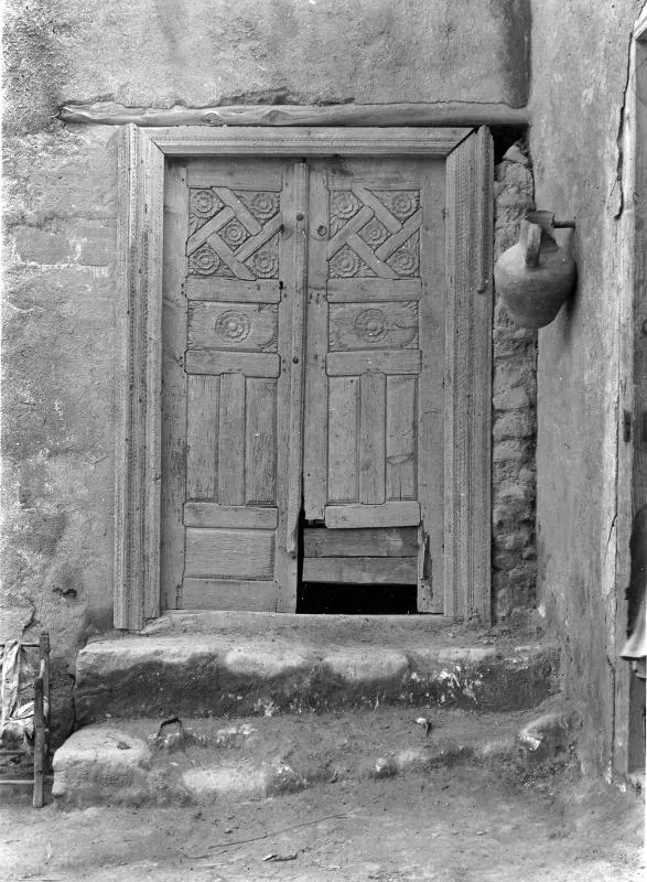 Carved wooden double door with rosette and lattice panels set in a plastered wall, with stone steps leading up to it