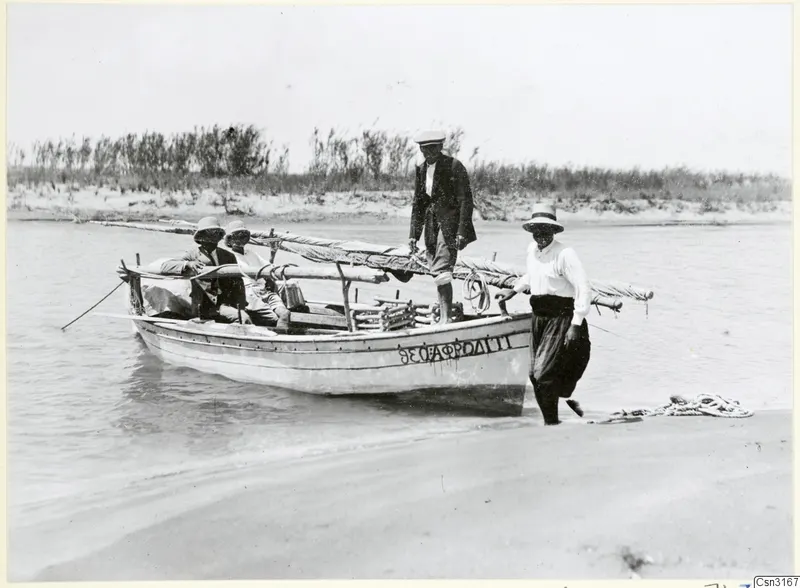 Small wooden boat with four people at the water's edge on a sandy shore