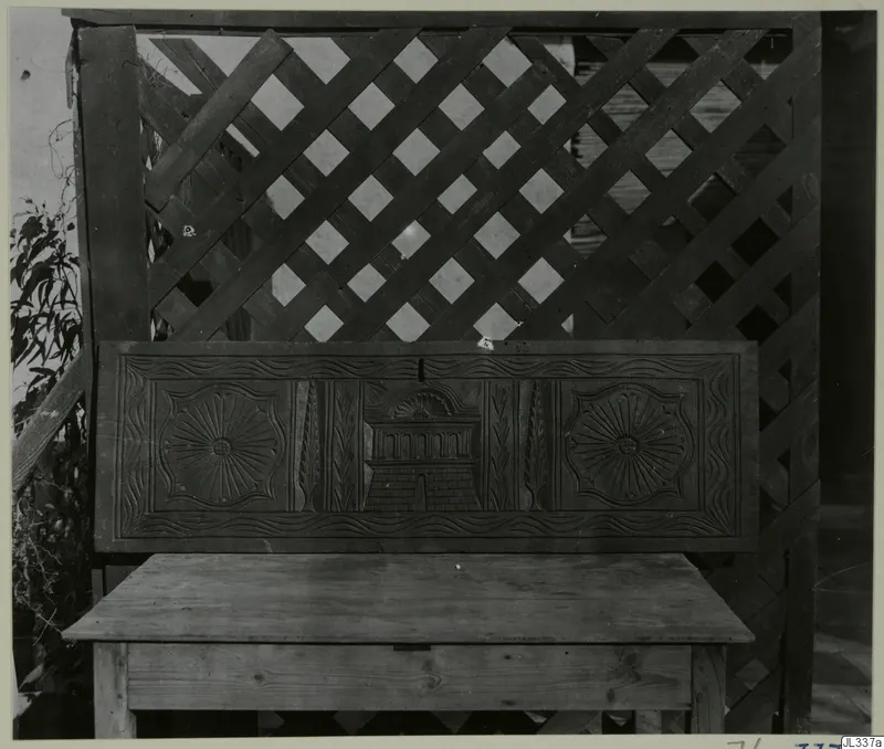 Carved wooden panel with two rosettes and a central arched motif, set above a low wooden box with a flat top