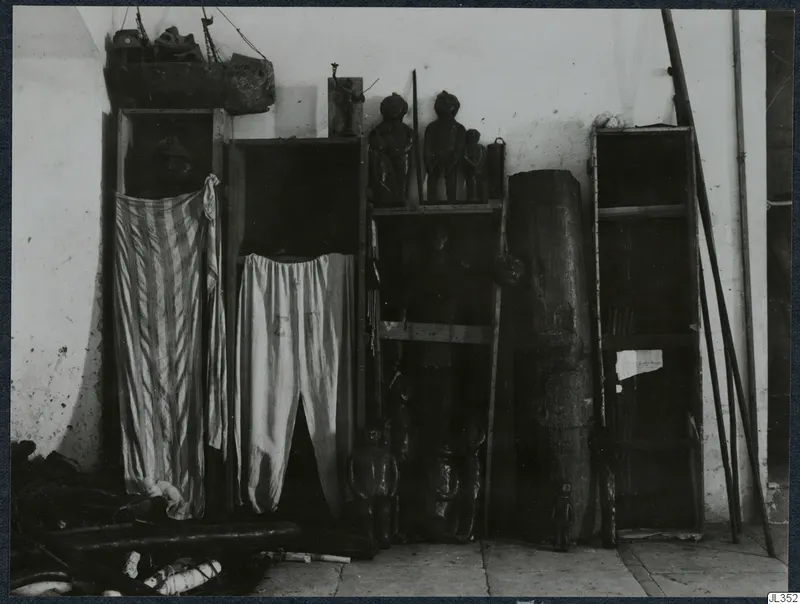 Wooden cupboards and shelves against a whitewashed wall, holding carved wooden figures and striped cloth