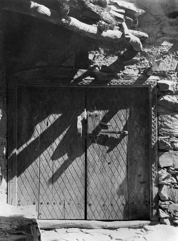 Wooden double door with a diagonal lattice pattern and iron fittings, set in a stone wall at Lazania