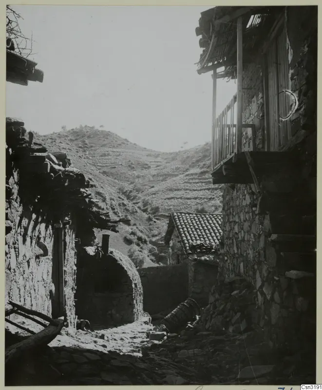 Stone village lane at Lazania with a wooden balcony on a stone house and terraced hills behind