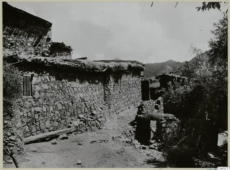 Stone-walled village lane at Lazanias, with tiled roofs and mountains rising behind the houses