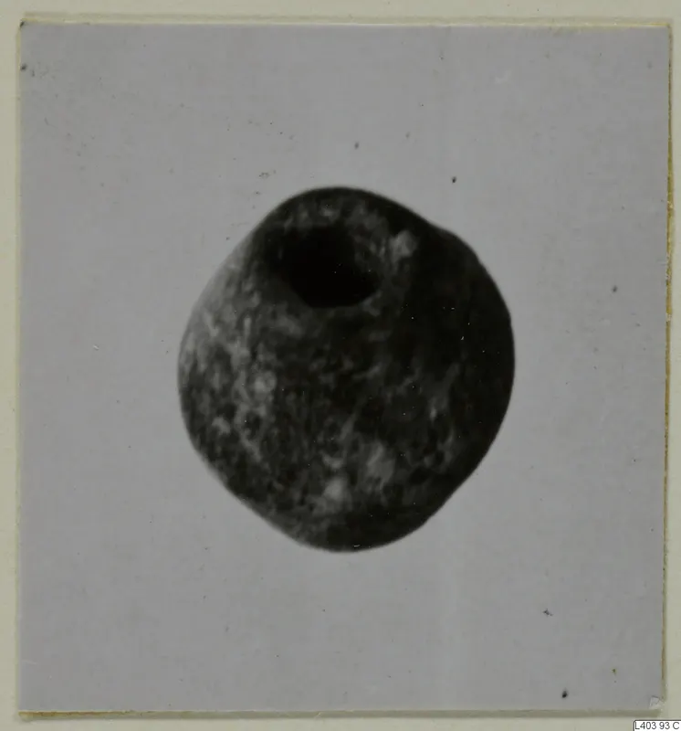 Rounded stone object with a large circular hole at the top, photographed on a pale card.