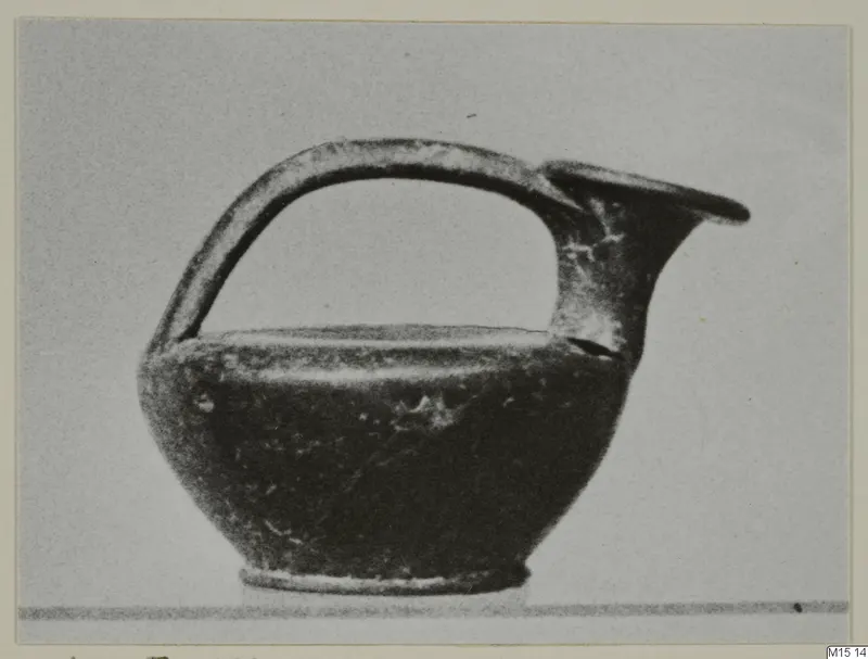 Small black-glazed jug with a strap handle and trefoil-like spout, photographed against a plain grey background.