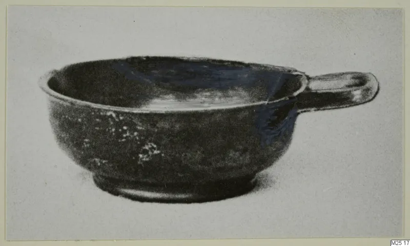 Black-glazed bowl with a single horizontal handle, shown in side view against a pale background.