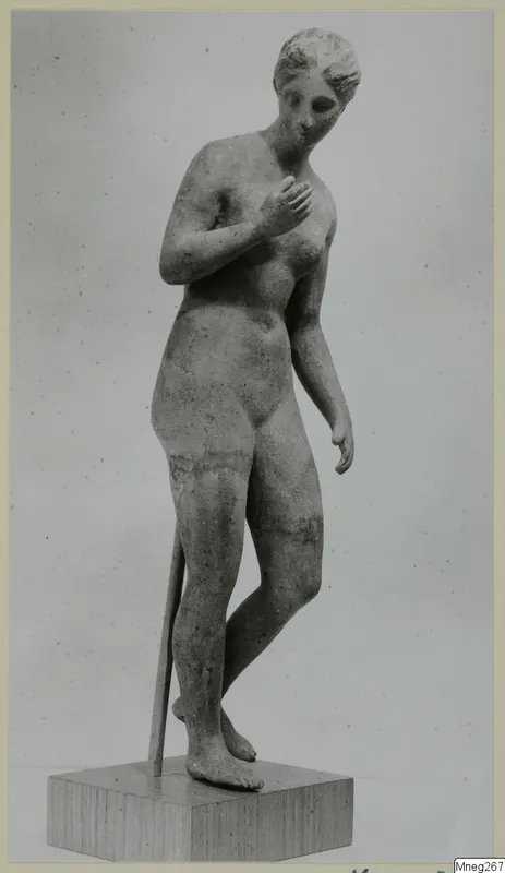 Standing nude statue of a female figure with one hand on her chest, on a wooden plinth