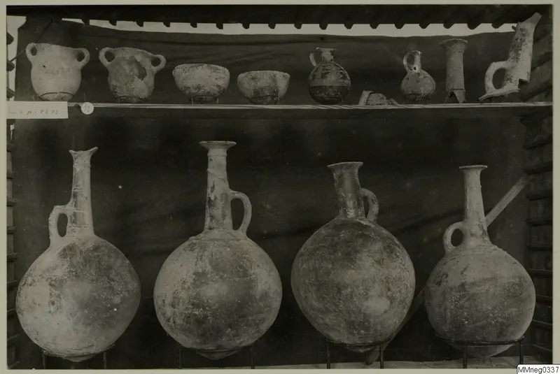 Pots, bowls and jugs displayed on two shelves against a dark cloth, from Lapithos Markides