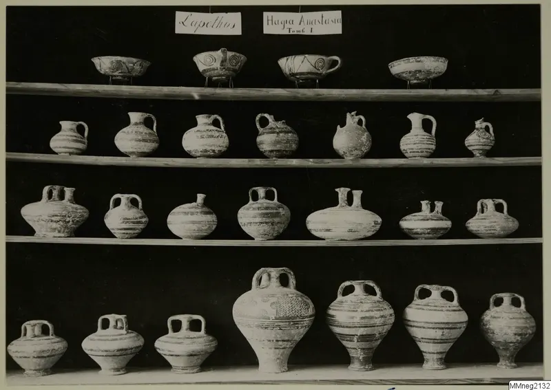 Pottery vessels from Lapithos Markides T.1 arranged in four rows on wooden shelves against a dark background