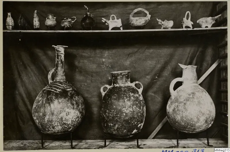 Three large pottery jars on metal stands, with small vessels on a shelf above, against a dark cloth backdrop
