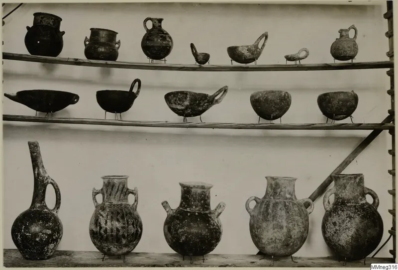 Pottery vessels from Cyprus on three wooden shelves: jugs, jars and bowls, several with geometric decoration.
