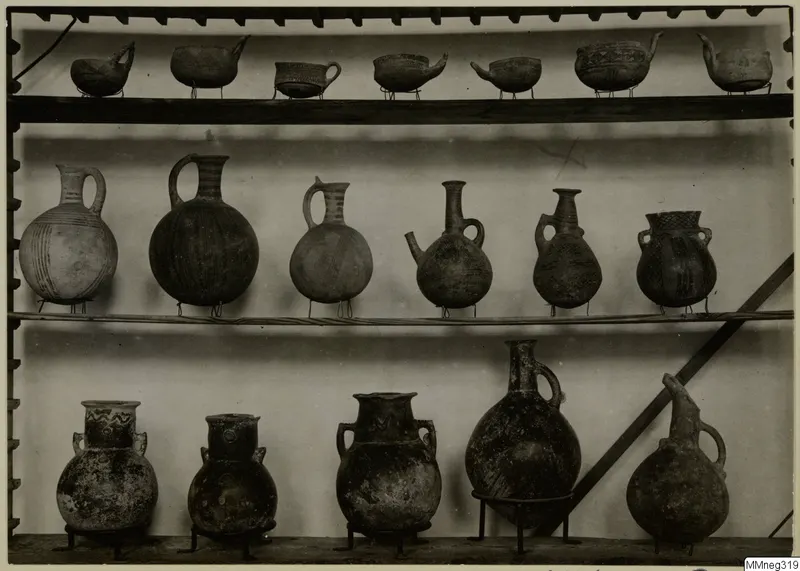 Shelves of pottery vessels on wire stands, including jugs, juglets and bowls with painted or incised patterns