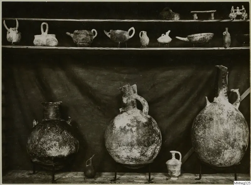 Pottery vessels on two shelves and metal stands in front of a draped dark cloth.