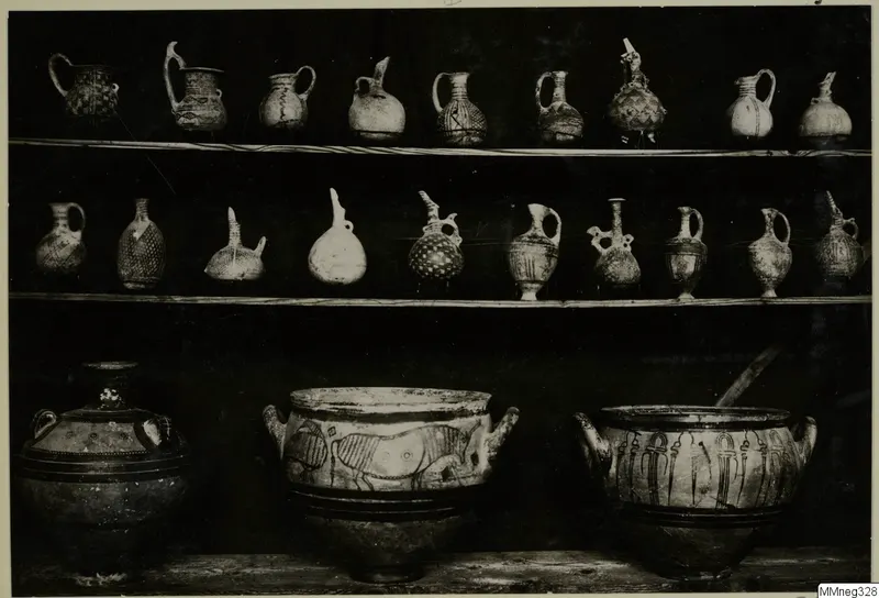 Three shelves of painted pottery jugs and jars, photographed against a dark background in a museum display.