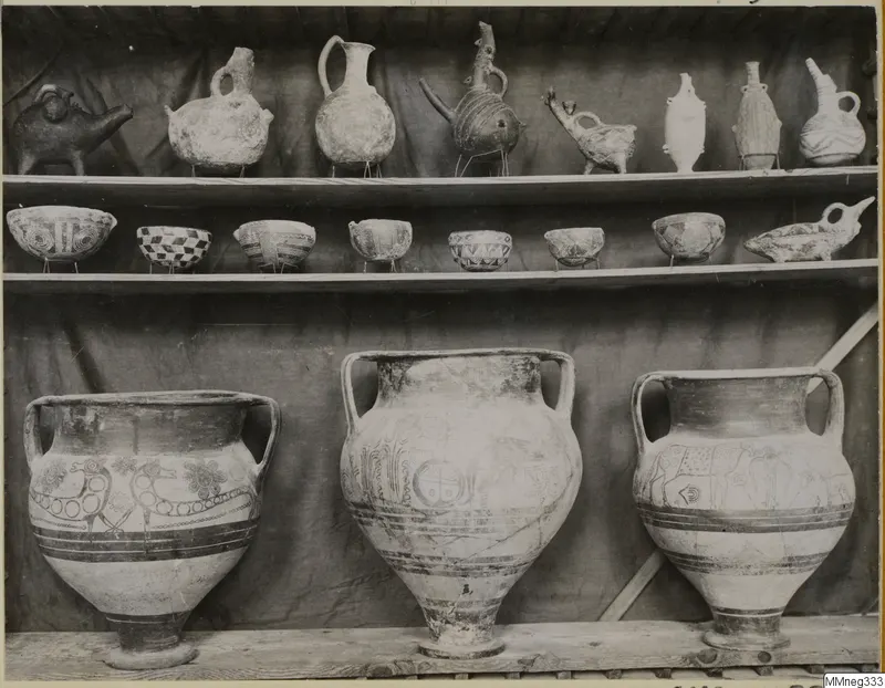 Shelves of painted pottery: animal-shaped and spouted vessels, seven small bowls, and three large two-handled jars